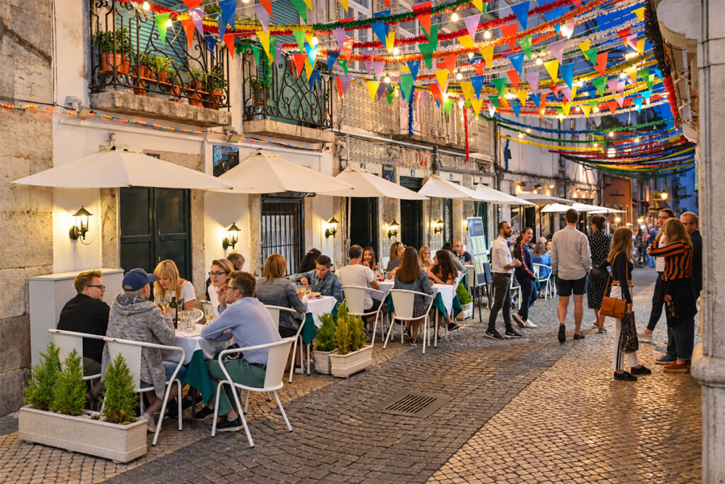 Diners at candlelit tables under bunting on a Bairro Alto street in the evening