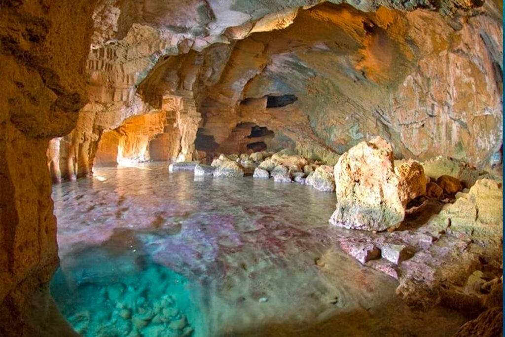 Inside the Cova Tallada, turquoise water pooling under the cave's carved rock ceiling