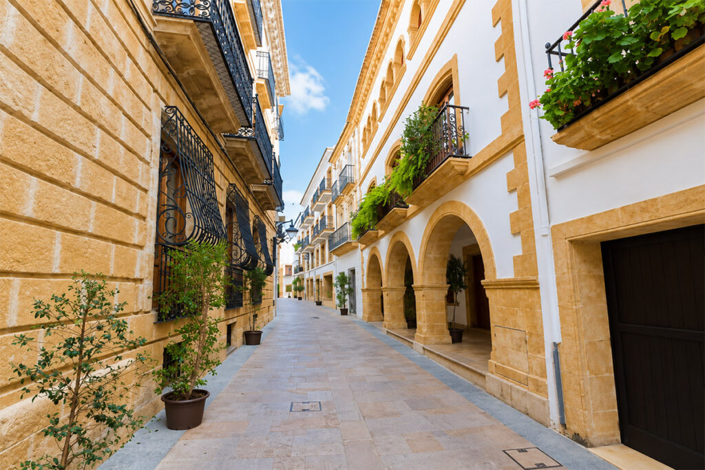 A stone street in the old town of Xàbia, arcades and flower-decked balconies