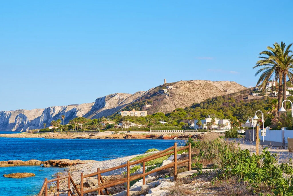 The rocky shore at Les Rotes, with the Torre del Gerro on the hill behind