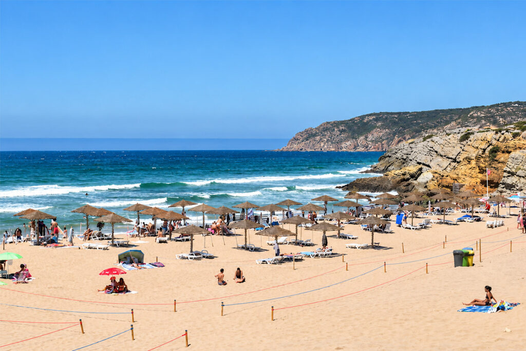 Beach umbrellas at Praia do Guincho, with the cliffs of the Serra de Sintra behind
